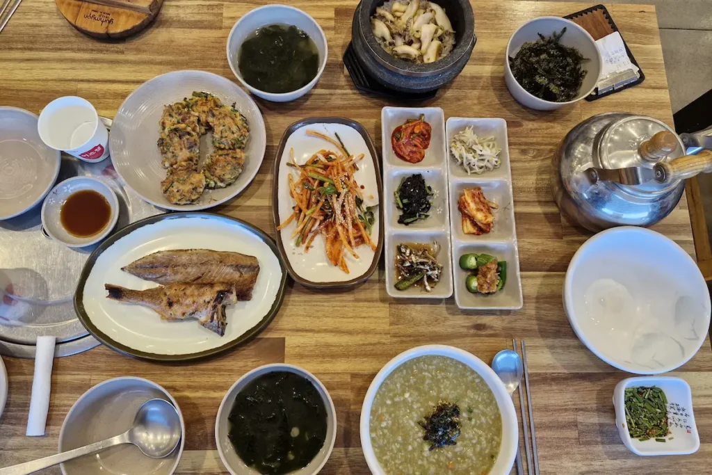 Abalone stone pot rice and abalone porridge served with grilled fish, seafood pancake, and Korean side dishes in Tongyeong.