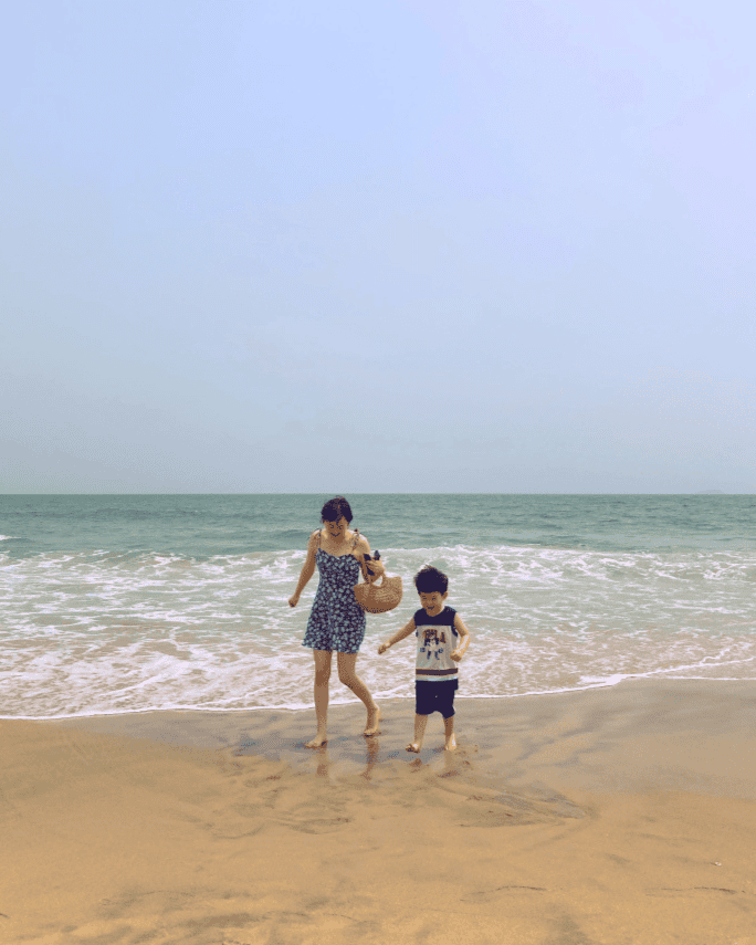Mother and child walking together on a beach during a family trip.