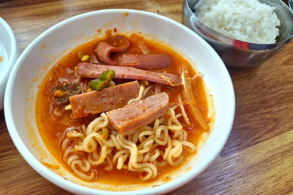 Close-up of Spam, sausage, and other ingredients simmering in spicy budae jjigae broth.