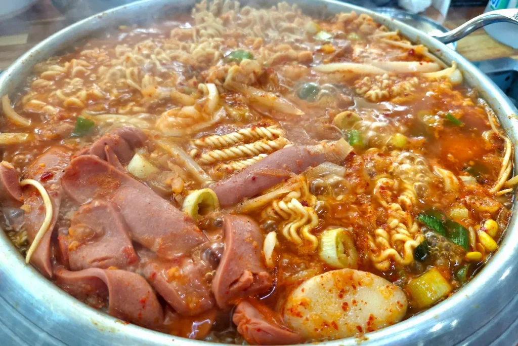 A bubbling pot of budae jjigae with Spam, sausage, kimchi, tofu, and vegetables.