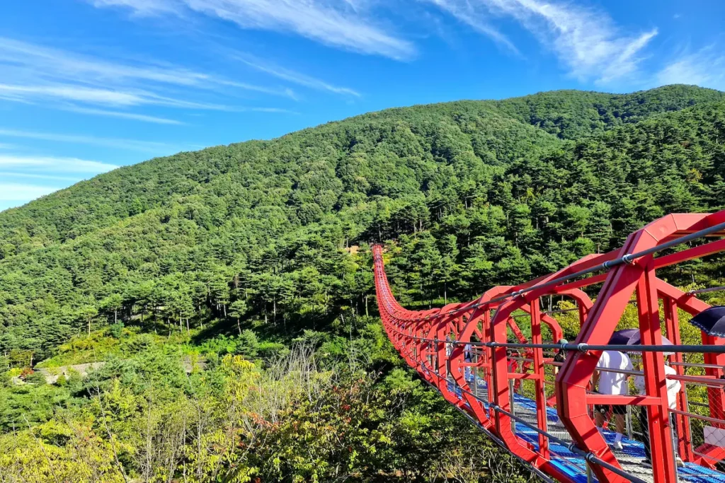 Red Mureung suspension bridge stretching across the forested mountains at Donguibogam Village in Sancheong.