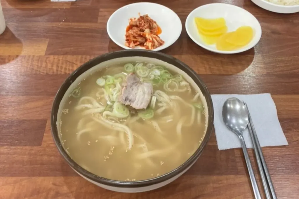 A bowl of Korean knife-cut noodles in savory meat broth topped with sliced meat and green onions in Geoje.