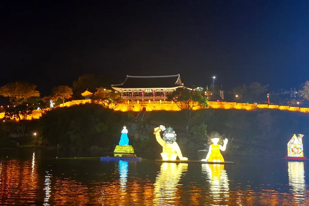 Illuminated lanterns floating on the Namgang River below Jinjuseong Fortress during the Jinju Namgang Yudeung Festival.