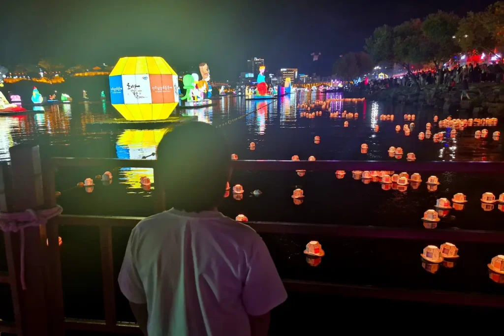 A child watching handmade wish lanterns floating on the Namgang River during the Jinju Namgang Yudeung Festival.