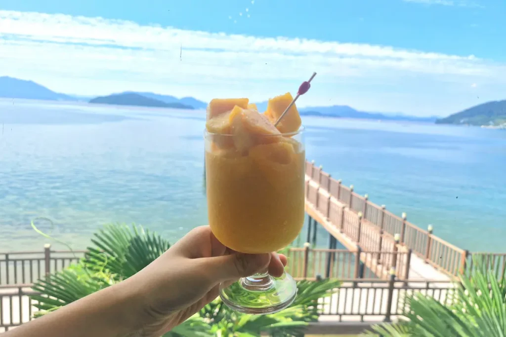 A mango drink with pieces of mango held in front of the sea at On the Sunset cafe in Geoje.