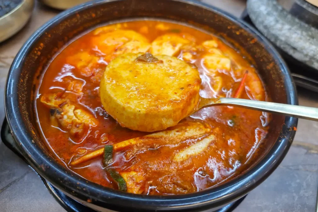 A spoonful of soft tofu lifted from a spicy bowl of Korean sundubu jjigae.