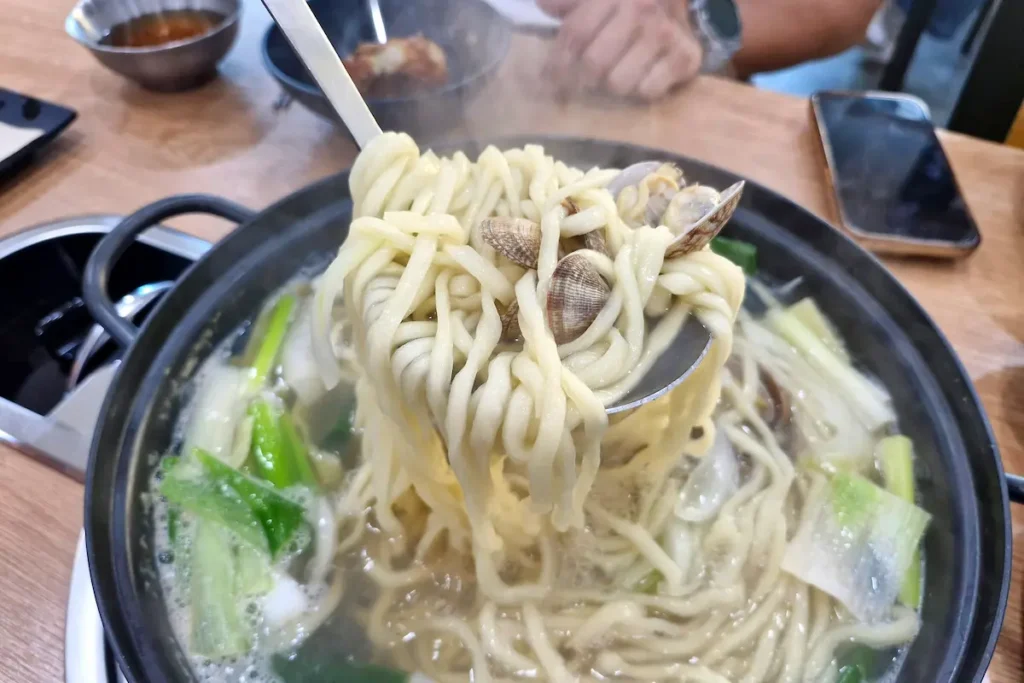 Korean knife-cut noodles with clams being lifted from a large bowl of kalguksu at Sommal Kalguksu in Gunsan.