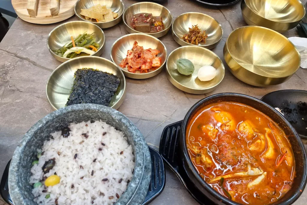 Korean sundubu jjigae served with rice, kimchi, seaweed, and several banchan side dishes.